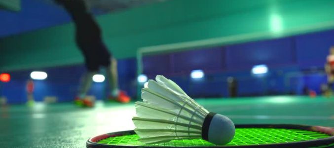 Close up low angle shot of hands of unrecognizable tennis player holding shuttlecock and racket while training on indoor court